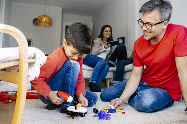 Father looking at son playing with toys in living room at home - JJF00931