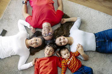 Smiling parents and children lying on carpet at home - JJF00933