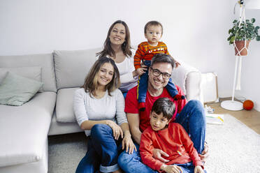 Smiling girl sitting with happy family in living room at home - JJF00936