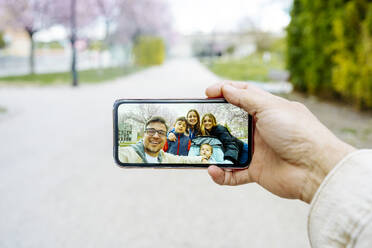 Ein Mann hält einen fröhlichen Moment mit seiner Familie im Park fest, indem er mit seinem Handy ein Selfie macht - JJF00949