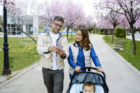 Mann teilt Smartphone mit Frau, die im Park auf dem Gehweg geht - JJF00951