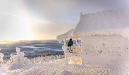 Frau sitzt auf der Veranda eines gefrorenen Hauses im Winter - LHPF01533