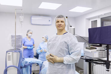 Chirurg mit Kollegen im beleuchteten Operationssaal - SANF00088