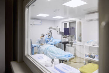 Doctor performing eye surgery in operating room seen through glass window - SANF00089