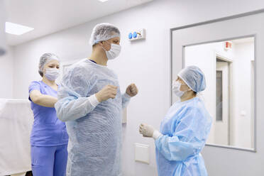 Doctor with colleagues preparing for surgery in operating room - SANF00090