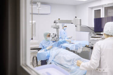 Ophthalmologist performing eye surgery in operating room seen through glass window - SANF00091