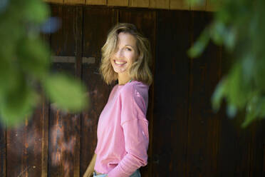 Happy blond woman outside wooden house - PNEF02770