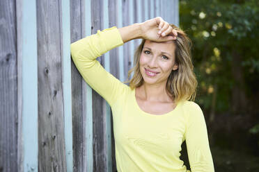 Smiling blond woman leaning on wall - PNEF02779