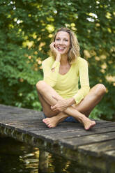 Smiling woman sitting cross-legged on boardwalk - PNEF02780