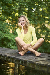 Blond woman sitting cross-legged on boardwalk - PNEF02782