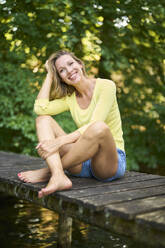 Happy mature woman sitting on boardwalk - PNEF02783