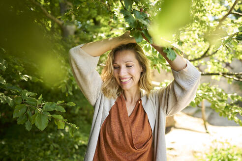 Lächelnde Frau hält Zweig eines Baumes - PNEF02789