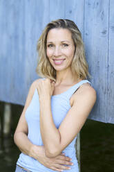 Smiling woman with blond hair leaning on wall - PNEF02797