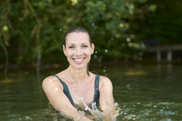 Glückliche Frau, die im See Wasser spritzt - PNEF02805