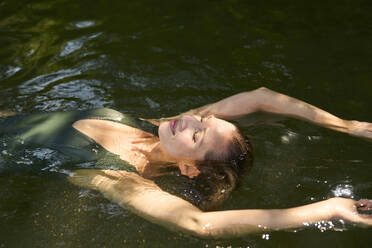 Unbekümmerte Frau mit erhobenen Armen, die auf dem Wasser eines Sees schwimmt - PNEF02806