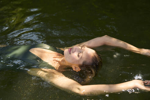 Carefree woman with arms raised floating on water in lake - PNEF02806