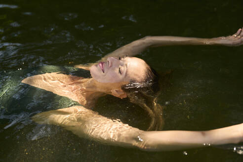 Smiling woman with eyes closed floating on water in lake - PNEF02807