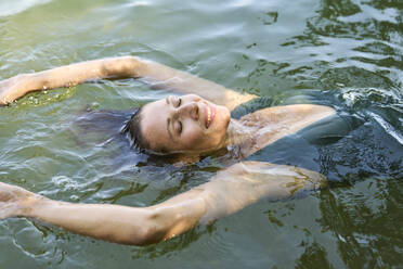 Lächelnde Frau schwimmt auf dem Wasser eines Sees - PNEF02808