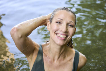 Happy woman with hand in hair enjoying in lake - PNEF02816