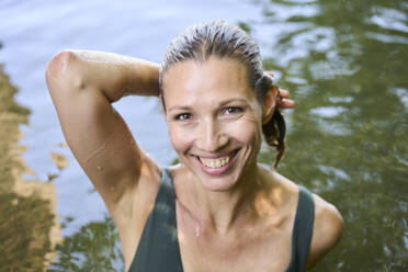 Happy mature woman with hand raised in lake - PNEF02817