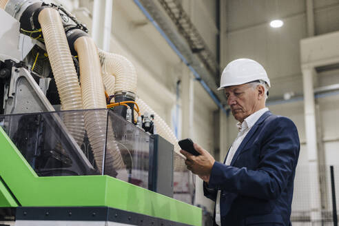 Geschäftsmann mit Smartphone in der Nähe einer modernen Maschine in der Industrie - JOSEF18675