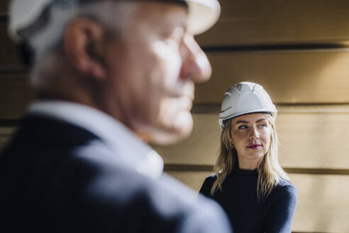 Businesswoman wearing hard hat with businessman in factory - JOSEF18704
