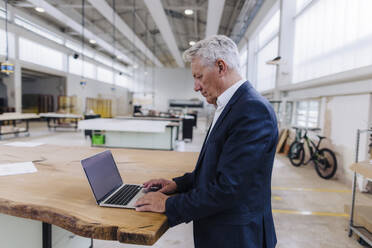 Businessman using laptop on workbench in factory - JOSEF18720