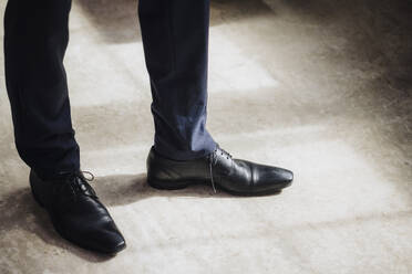 Beine eines Geschäftsmannes mit schwarzen formellen Schuhen, der in einer Fabrik steht - JOSEF18724