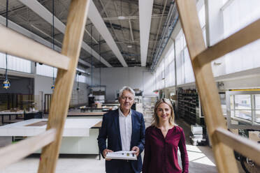 Lächelnde Geschäftsfrau und Geschäftsmann betrachten eine Holzkonstruktion in einer Fabrik - JOSEF18737