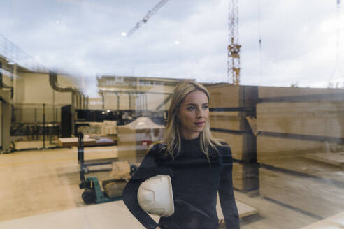 Businesswoman standing in factory seen through glass - JOSEF18750