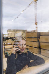 Businesswoman talking on smart phone in factory seen through glass - JOSEF18751