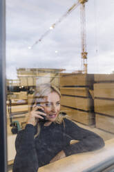 Geschäftsfrau, die in einer Fabrik mit einem Smartphone telefoniert, gesehen durch Glas - JOSEF18751