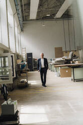Senior businessman walking on production floor in factory - JOSEF18819