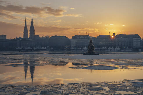 Germany, Hamburg, Ice floating in Alster Lake at sunset with city skyline in background - KEBF02714