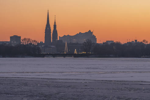 Germany, Hamburg, Ice floating in Alster Lake at dusk with city skyline in background - KEBF02718