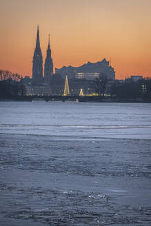 Germany, Hamburg, Ice floating in Alster Lake at dusk with city skyline in background - KEBF02719