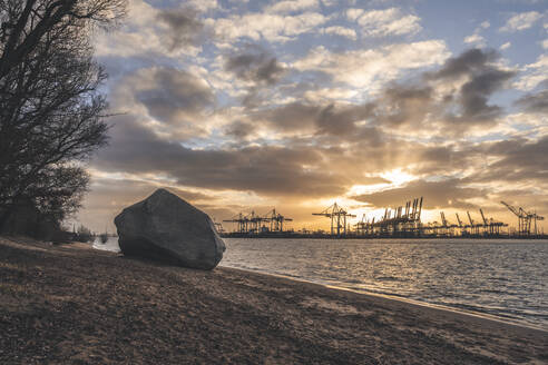 Deutschland, Hamburg, Elbstrand bei bewölktem Sonnenaufgang mit Hamburger Hafen im Hintergrund - KEBF02726