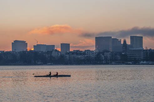 Deutschland, Hamburg, Alstersee in der Morgendämmerung mit Stadtsilhouette und Ruderboot im Hintergrund - KEBF02730