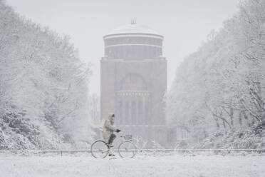 Germany, Hamburg, Person riding bicycle past Stadpark planetarium during heavy snowfall - KEBF02742
