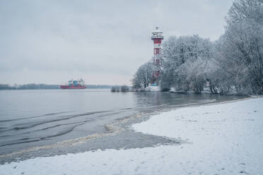 Deutschland, Hamburg, Schneebedecktes Elbufer mit Leuchtturm Wittenbergen im Hintergrund - KEBF02743