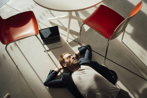 Geschäftsmann entspannt auf dem Boden mit Laptop und Stühlen im Büro - JOSEF18883