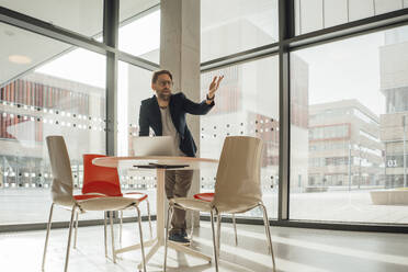 Businessman video conferencing on laptop by glass window in office - JOSEF18884