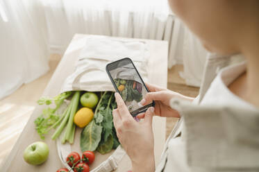 Frau fotografiert zu Hause Lebensmittel mit dem Smartphone - ALKF00269