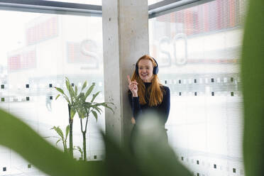 Businesswoman wearing headphones and gesturing in office - JOSEF18943