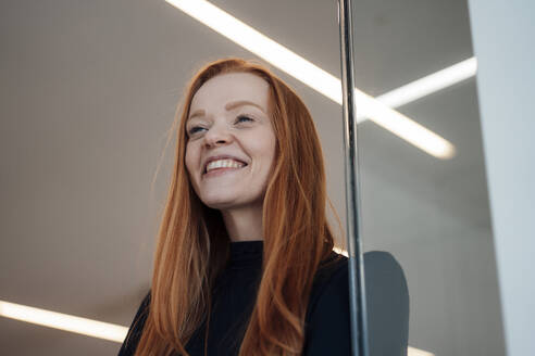 Happy redhead businesswoman near wall at office - JOSEF18950