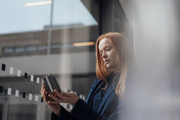 Redhead businesswoman analyzing machine part at window - JOSEF18959