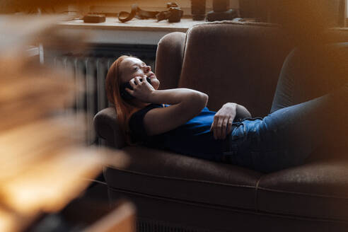 Frau, die auf dem Sofa liegend durch ihr Smartphone spricht - JOSEF19009