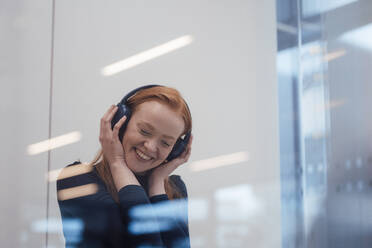 Happy woman enjoying listening to music behind window - JOSEF19024