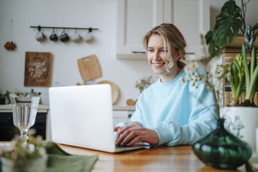 Lächelnde Frau mit Laptop auf dem Esstisch zu Hause - MDOF01056