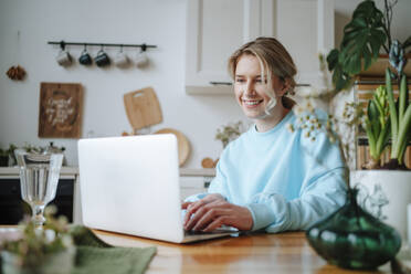 Smiling woman using laptop on dining table at home - MDOF01056